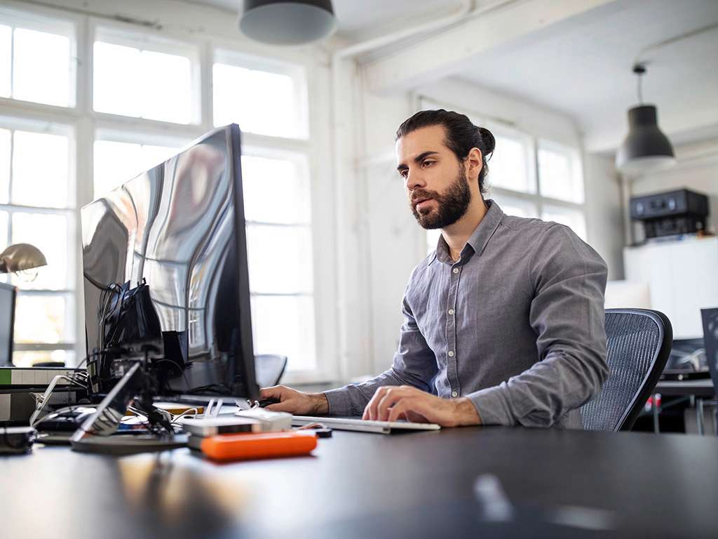 Hombre con pelo largo peinado y trabajando en oficina frente a computador 